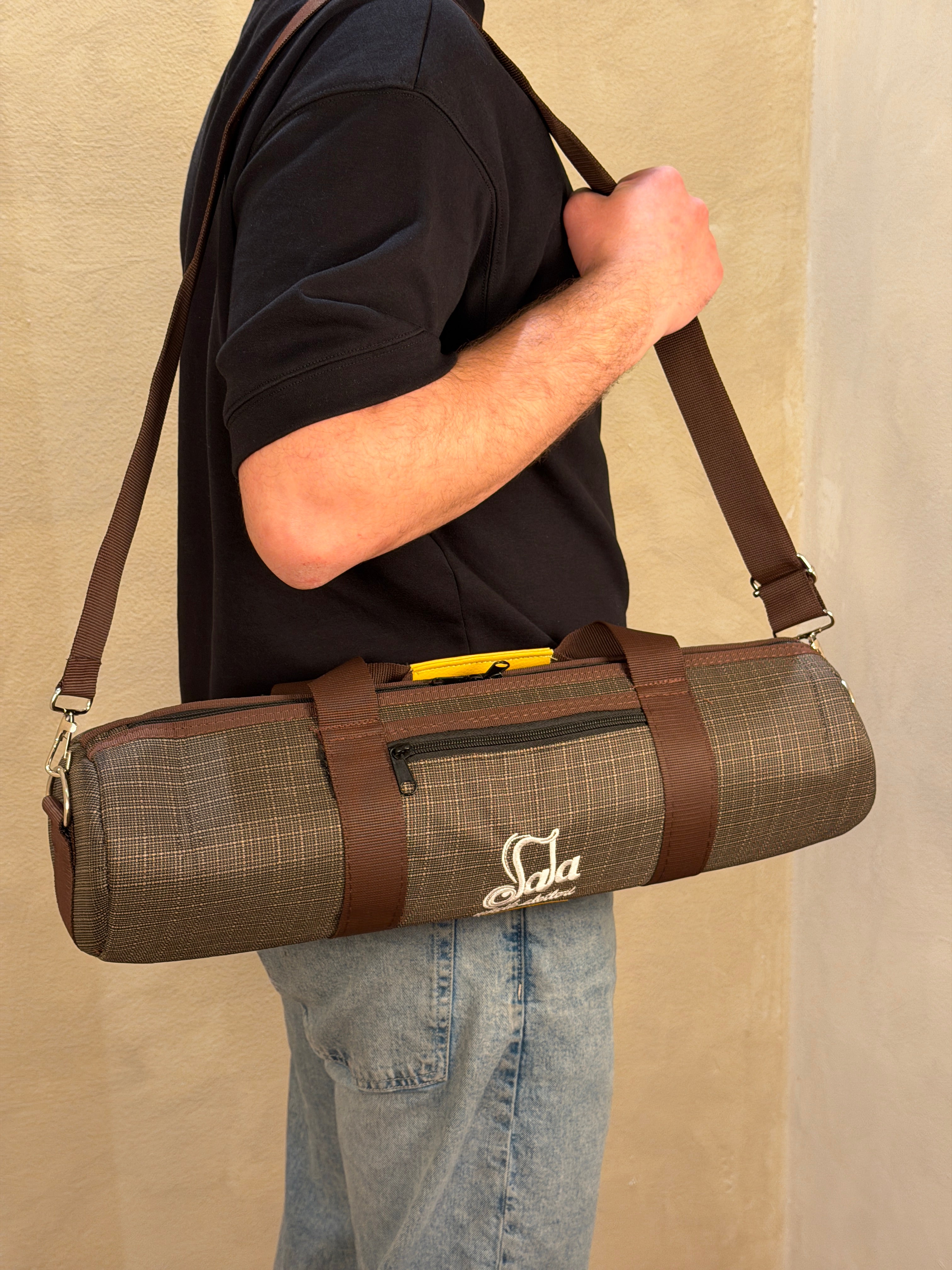 Person holding a duduk case with a carrying strap on a beige surface