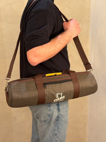 Person holding a duduk case with a carrying strap on a beige surface