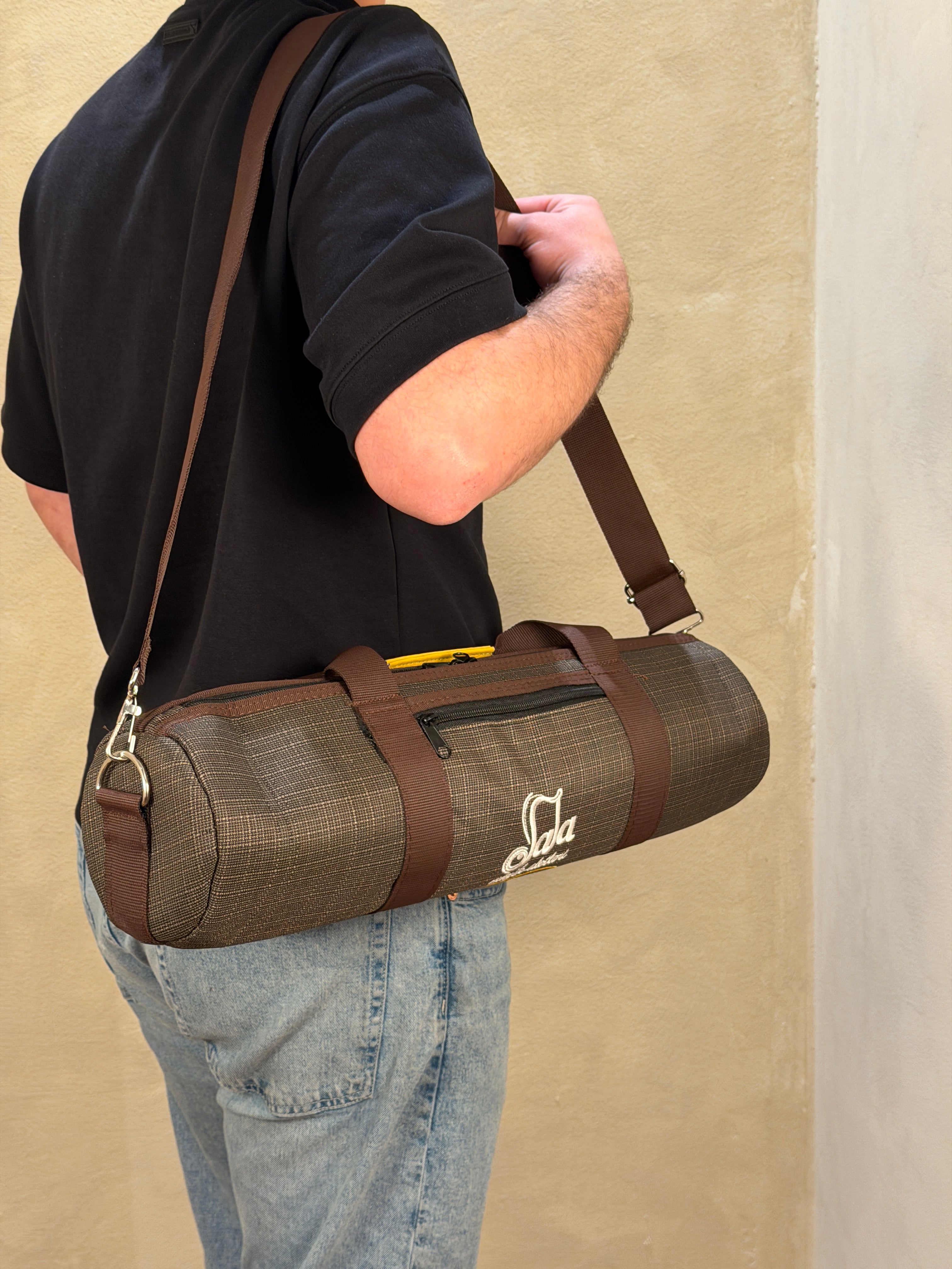 Person holding a zurna case with a carrying strap on a beige floor.